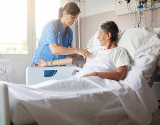 Photo with copy space of female nurse leaning over bedside while attaching the blood pressure armband to a female patient's right arm.